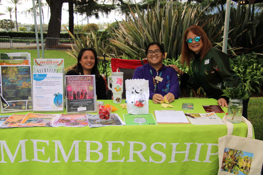three people seated behind a booth with a green tablecloth that reads membership on their table