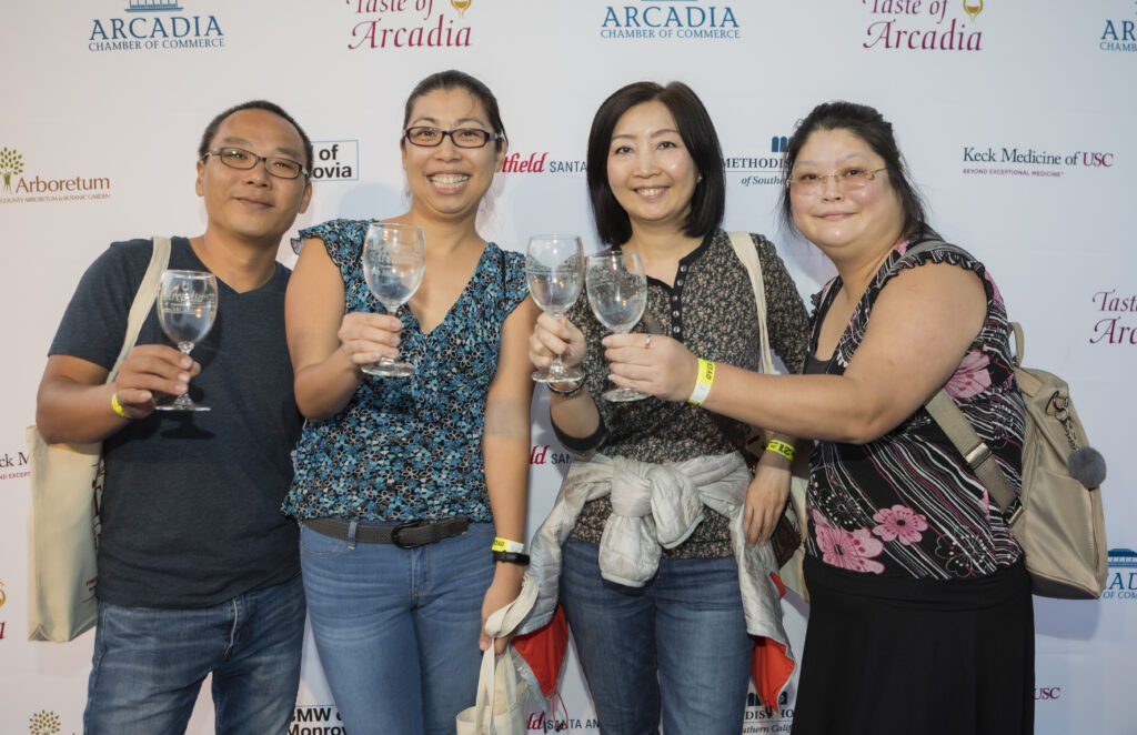 three women and a man standing in front of a step and repeat banner holding wine glasses