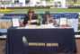 two women sitting behind a booth with a blue table cloth reading Downtown Arcadia