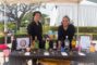 a woman and a man in black behind a booth set with a black cloth and displays of liquor