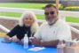 a woman in black with white hair and a man in white wearing sunglasses seated at a booth for Mohajer Law