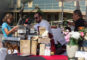 a man in white handing a sample to a woman in a blue shirt at a booth for Domenico's