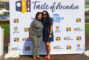 a woman in a gray suit and a woman in a blue dress standing in front of a step and repeat banner