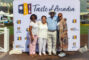 three women standing with a man in a blue shirt and white hat in front of a step and repeat banner for Taste of Arcadia