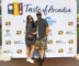 a woman in a patterned dress and a man in plaid shorts standing in front of a step and repeat banner for Taste of Arcadia