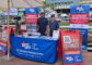 two men in blue shirts standing behind a booth featuring information on Western Rooter