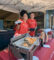 a woman and a man in red USC Arcadia Hospital shirts behind a booth with chafers of sliders
