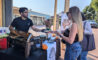 a man in a black shirt at a Twohey's booth handing food to a woman with long blonde hair