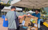 a man in a blue Mt Lowe shirt handing a beer to a man in a gray shirt who we can only see from behind