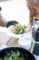 a salad on a white plate behind held out by a hand wearing a black glove
