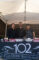 three men standing behind a booth set with a table cloth showing the Derby logo