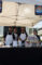 a group of a woman and three men all wearing black shirts and white aprons behind a table set with a black table cloth