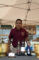 a man in a red D A'quino shirt standing behind a table set with wines