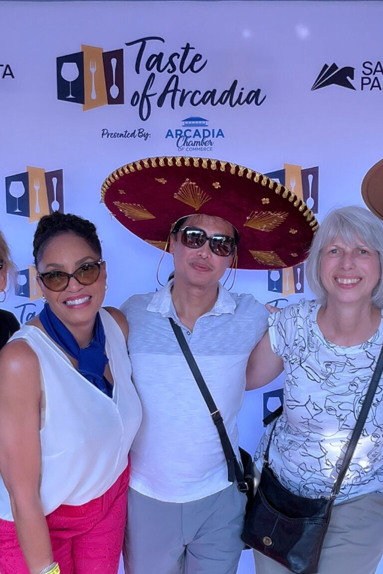 a large group of people with a woman in the middle wearing a straw hat in front of a Taste of Arcadia backdrop