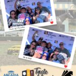 a large group of people holding signs in a photo booth on a background with the Taste of Arcadia logo