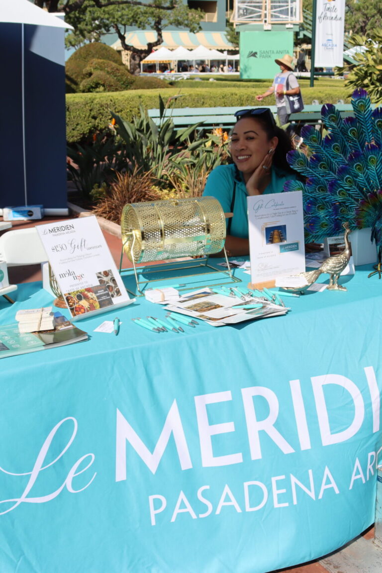 a woman in a turquoise t-shirt sits behind a table with a Le Meridien table cloth in the same turquoise color