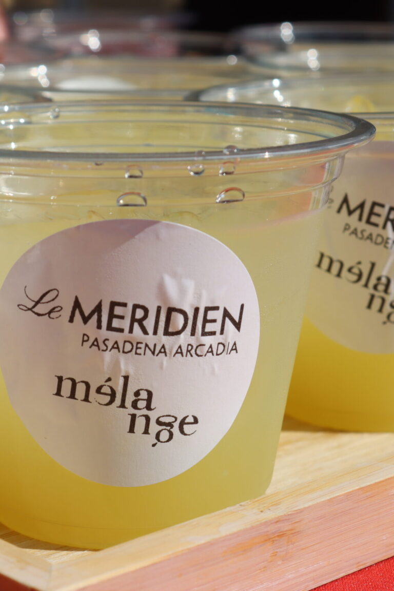 a grouping of plastic cups with the Le Meridien Melange logo on them, filled with a yellow colored cocktail