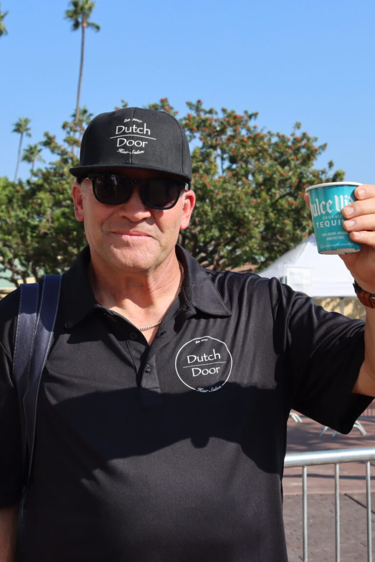 a man in a black polo and hat with the Dutch Door logo on it holds up a blue Dulce Vida cup