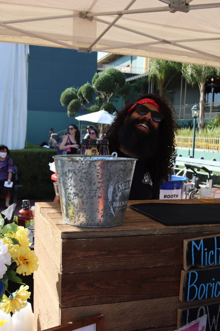 a man with curly hair and beard smiles from behind a bar set up for Mt Lowe Brewing Co