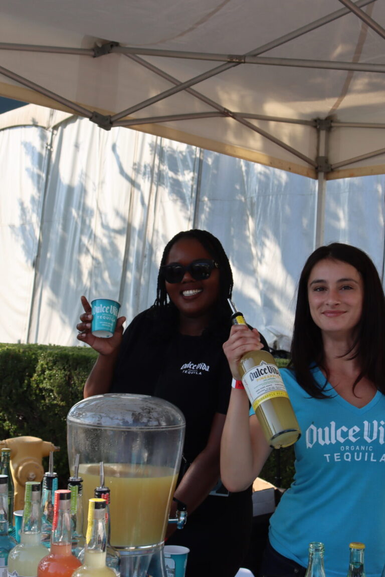 a woman in a blue shirt holding a bottle of Dulce Vida tequila while a woman in a black shirt holds a blue Dulce Vida cup
