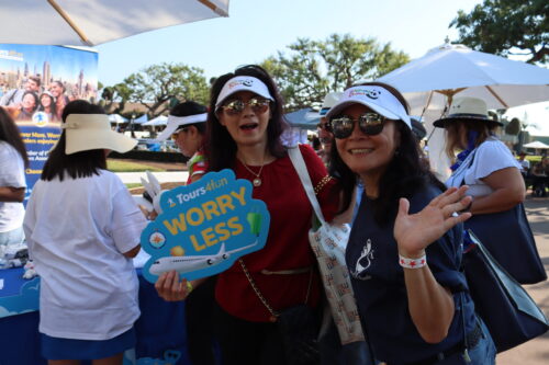 a woman in red shirt holds a sign saying 'tours4Fun, worry less' while a woman in a blue shirt beside her waves at the camera