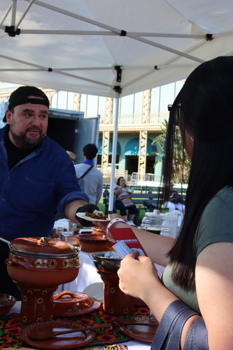 a man in a blue Girasol shirt and backwards cap hands a plate of food to two women