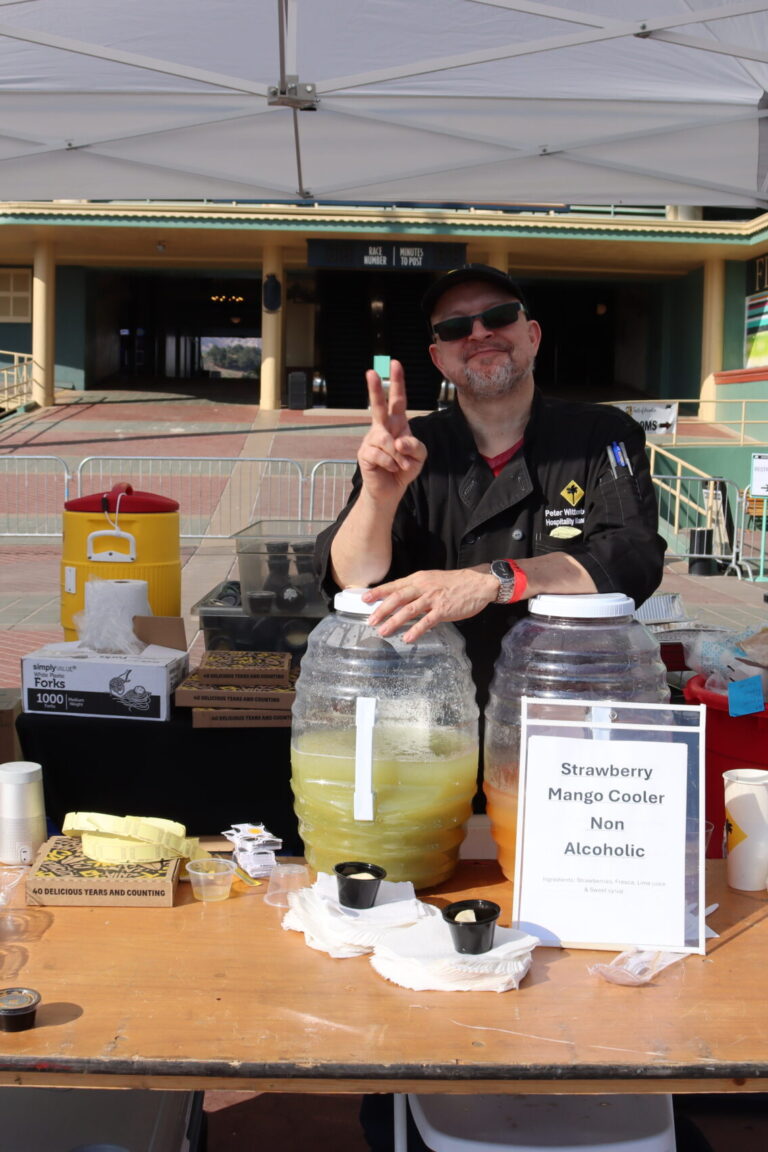 a man giving a peace sign behind a table set with jars of agua fresca