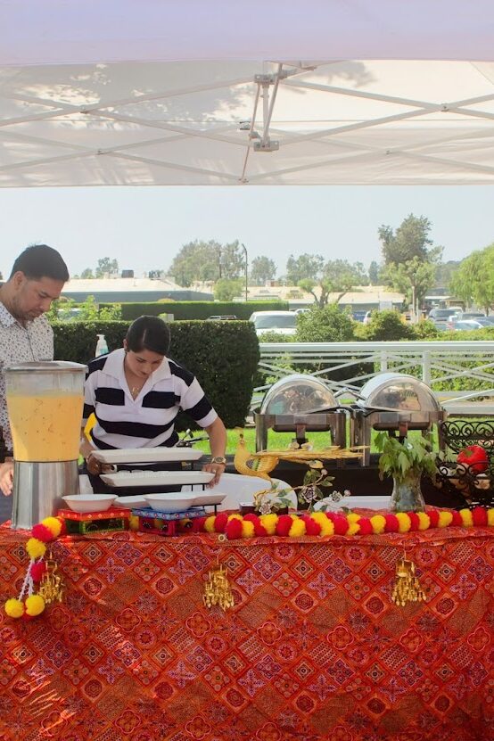 a booth for All India Cafe set with red and gold flowers, a red table cloth, and a sign for catering from the restaurant