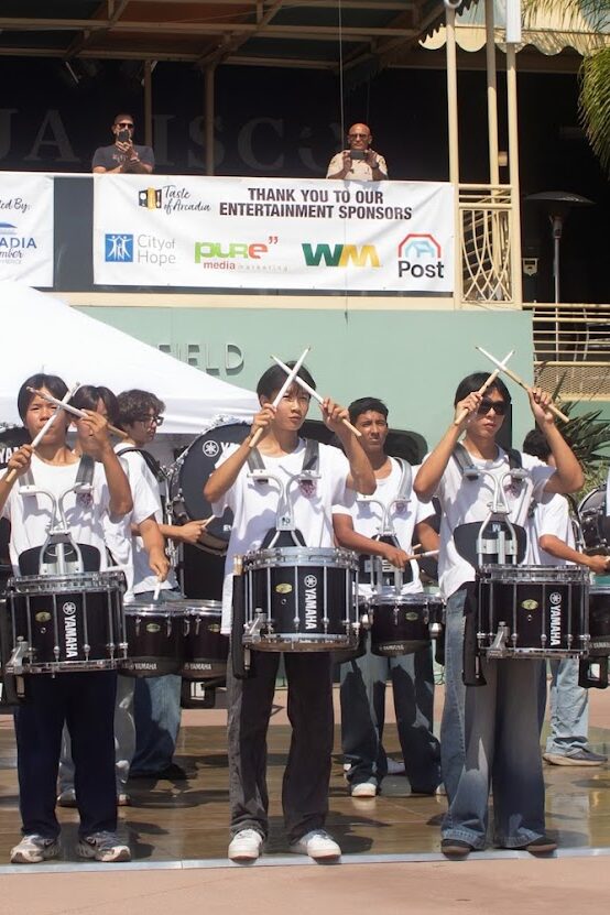 the Arcadia High School drumline standing on a dance floor with their sticks crossed in the air in front of them