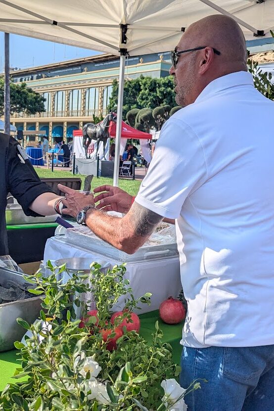 a man in a white shirt being handed a cup of food from a man in a black shirt and black hat while a woman in a black shirt watches