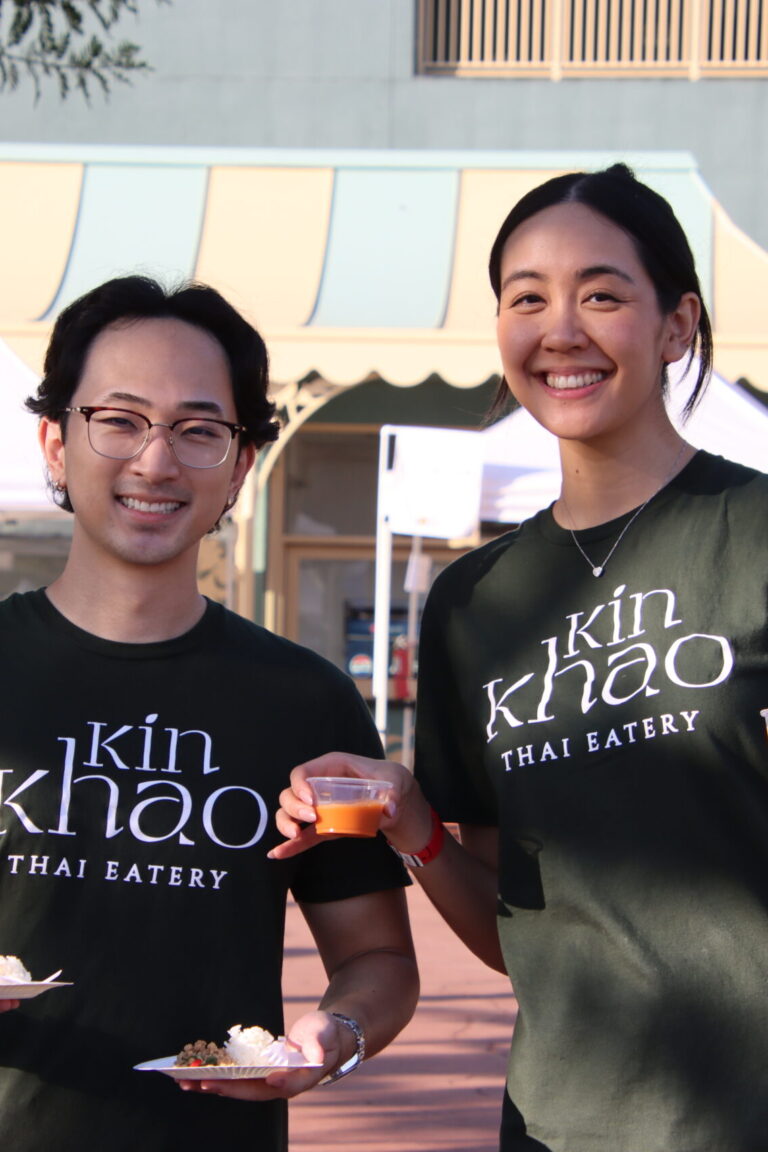 a woman and a man in Kin Khao t shirts holding up food and drink at Taste of Arcadia