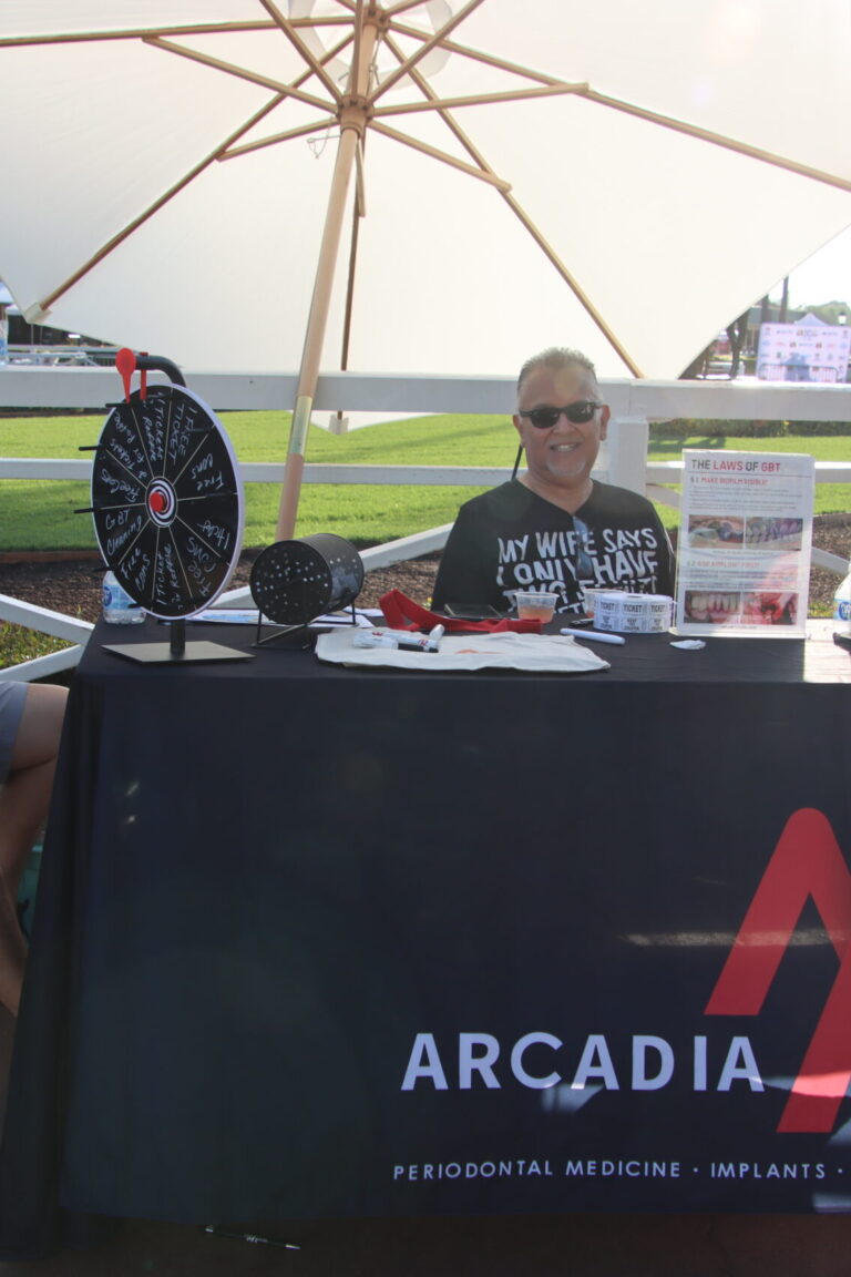 a woman standing behind a booth for Arcadiaperio with two men seated beside her, at Taste of Arcadia