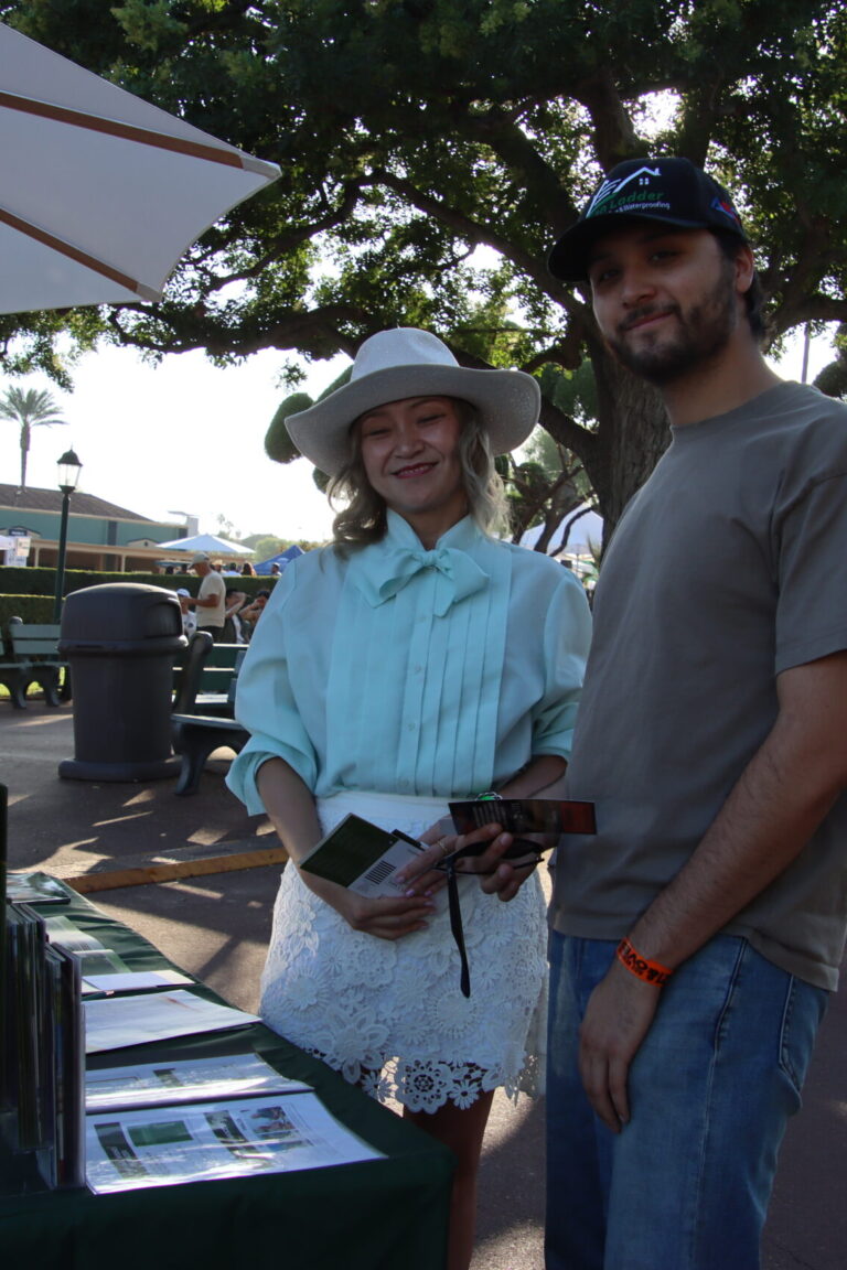 a woman in a blue shirt standing by a man wearing a green ladder hat at a booth for Forest Lawn