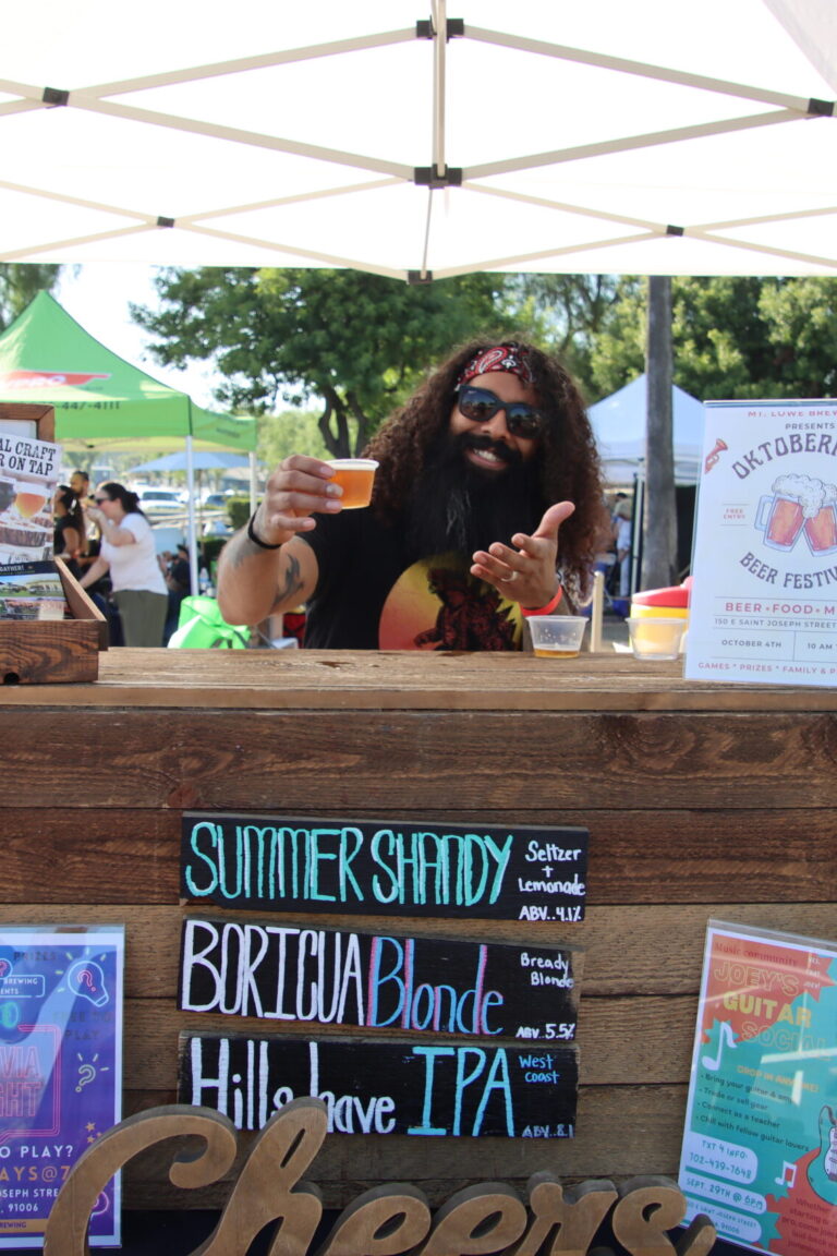a man with curly hair and a beard holding out a sample of beer at the Mt Lowe booth at Taste of Arcadia