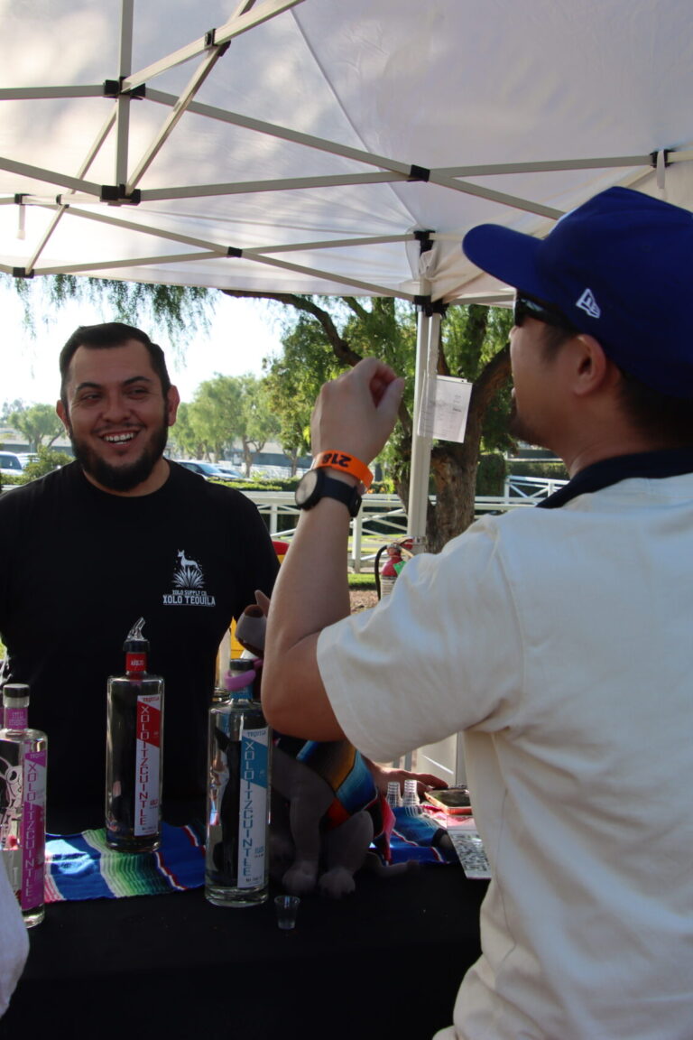 a man behind a booth for Xolo Tequila with two people in front of him taking drinks at Taste of Arcadia