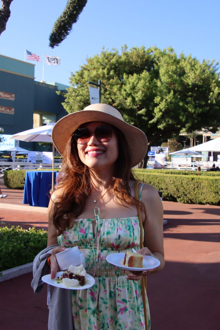a woman in a green dress and sunhat holding multiple plates of food
