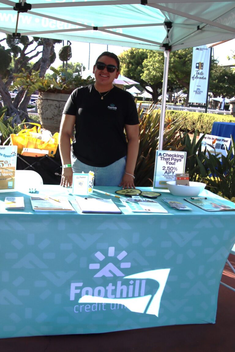 a man standing behind a booth for the Foothill Credit Union at Taste of Arcadia