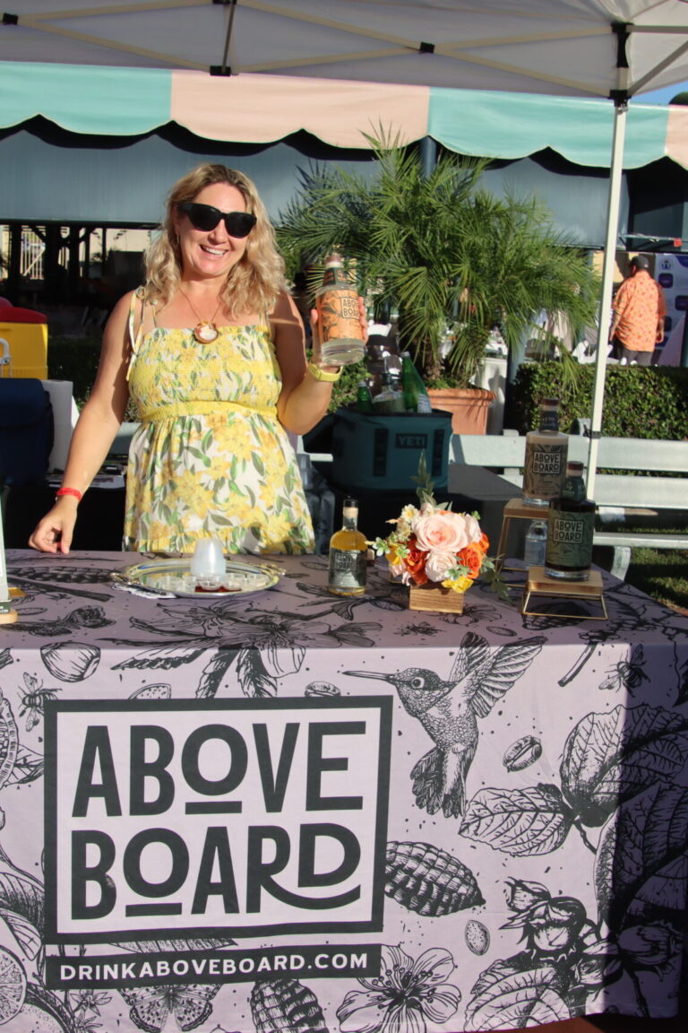 a woman holding a bottle of liquor behind a booth set for Above Board liquors at Taste of Arcadia